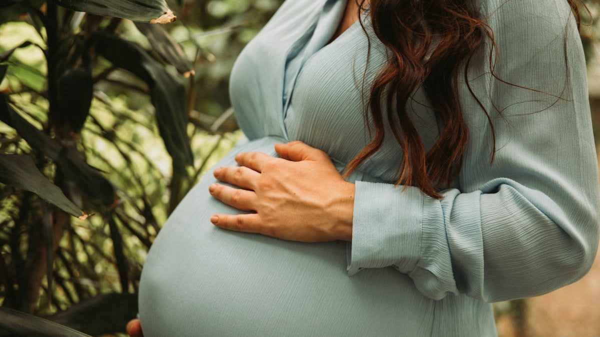 a pregnant woman standing in front of a tree
