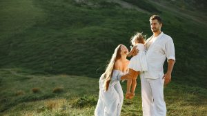 A joyful family of three in white clothing enjoying the outdoors on a sunny day.