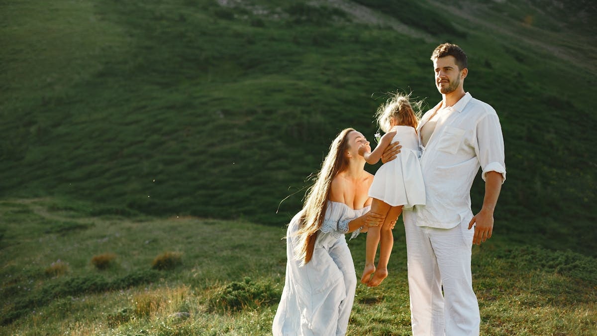 A joyful family of three in white clothing enjoying the outdoors on a sunny day.